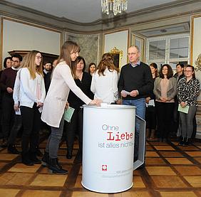 Mitarbeiterinnen und Mitarbeiter der Caritas übergeben ihre Umschläge mit „Herzenswünschen“ der Caritas-Spendendose