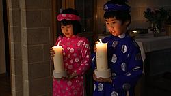 Zwei Kinder in traditionellem vietnamesischen Gewand tragen eine Kerze zum Altar. Sie schauen bedächtig. 