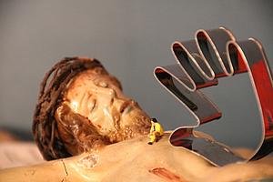 Liegende Christusfigur mit kleiner Menschenfigur auf der Brust und eine symbolischen Hand