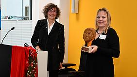 Die 3. Bürgermeisterin von Weißenburg, Katrin Schramm (links), überreichte Caritas-Kreisstellenleiterin Alexandra Trögl zum Einzug eine Römermaske aus Stahl, ein Wahrzeichen der Stadt Weißenburg. 