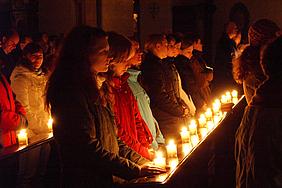 Menschen mit Kerzen in einer Kirchenbank.