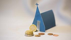 Symbolbild: Geldmünzen vor kleiner blauer Kirche