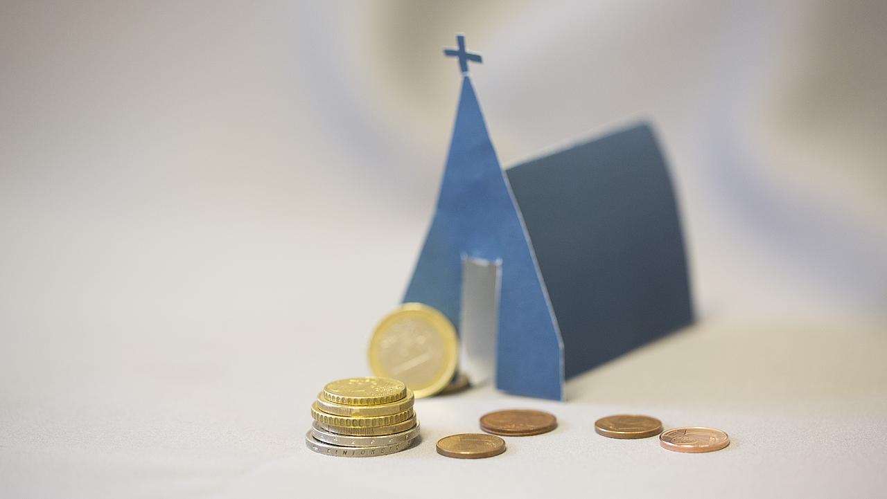 Kleine Kirche aus Papier mit Geldstücken davor