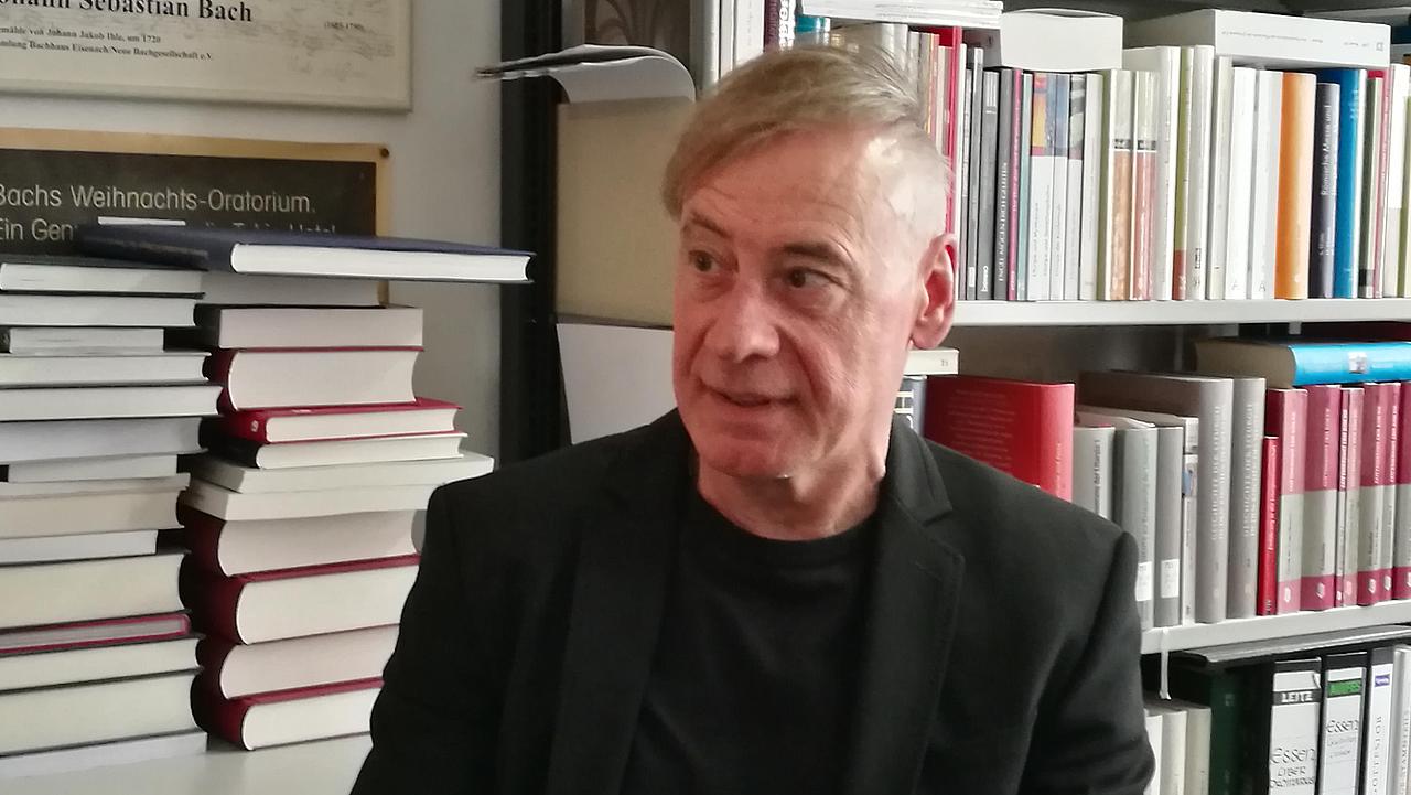 Jürgen Bärsch sitzt vor einem Bücherregal. 