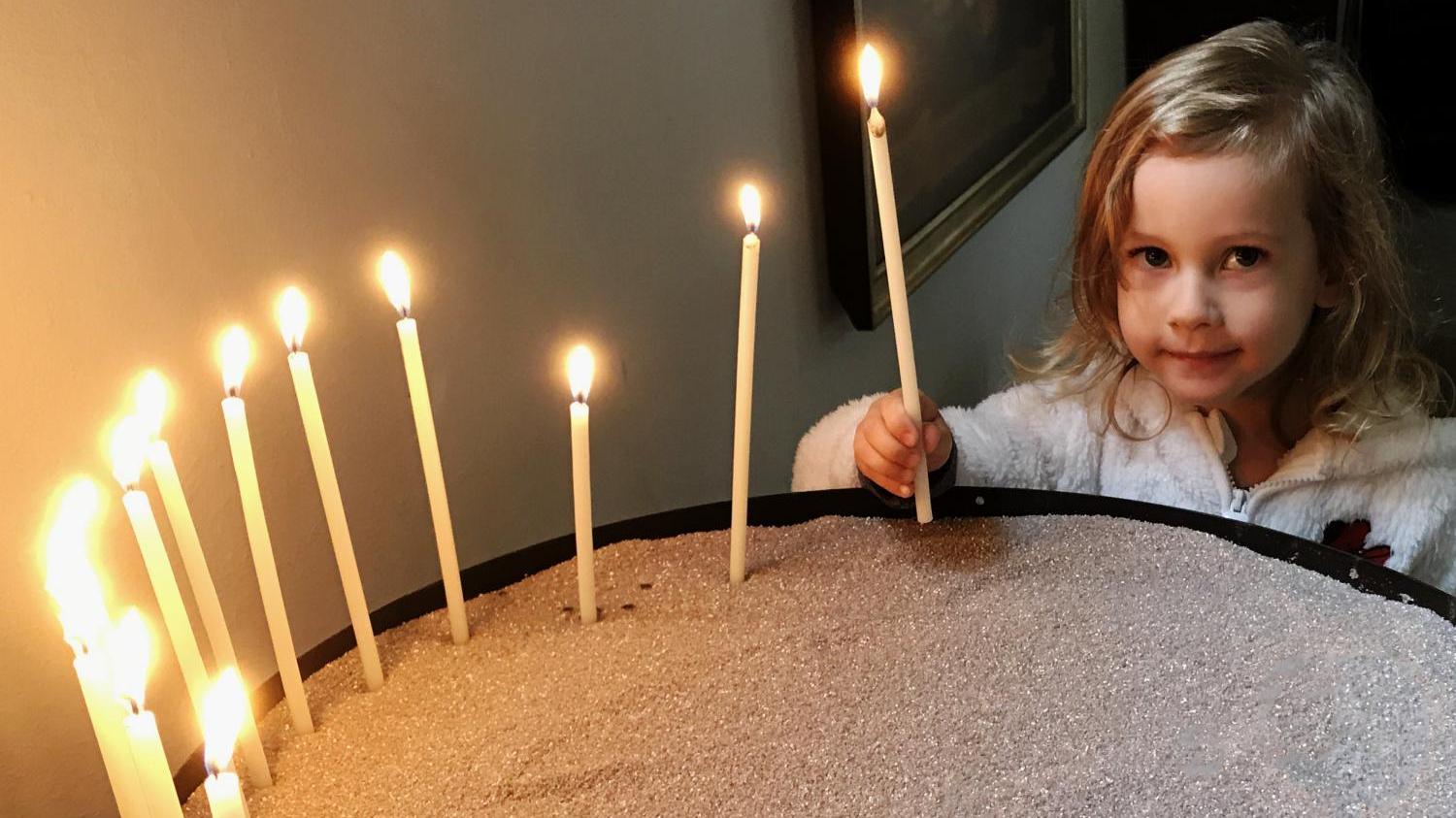 Mädchen entzündet Kerze in einer Kirche.