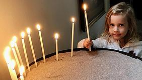 Mädchen entzündet Kerze in einer Kirche.