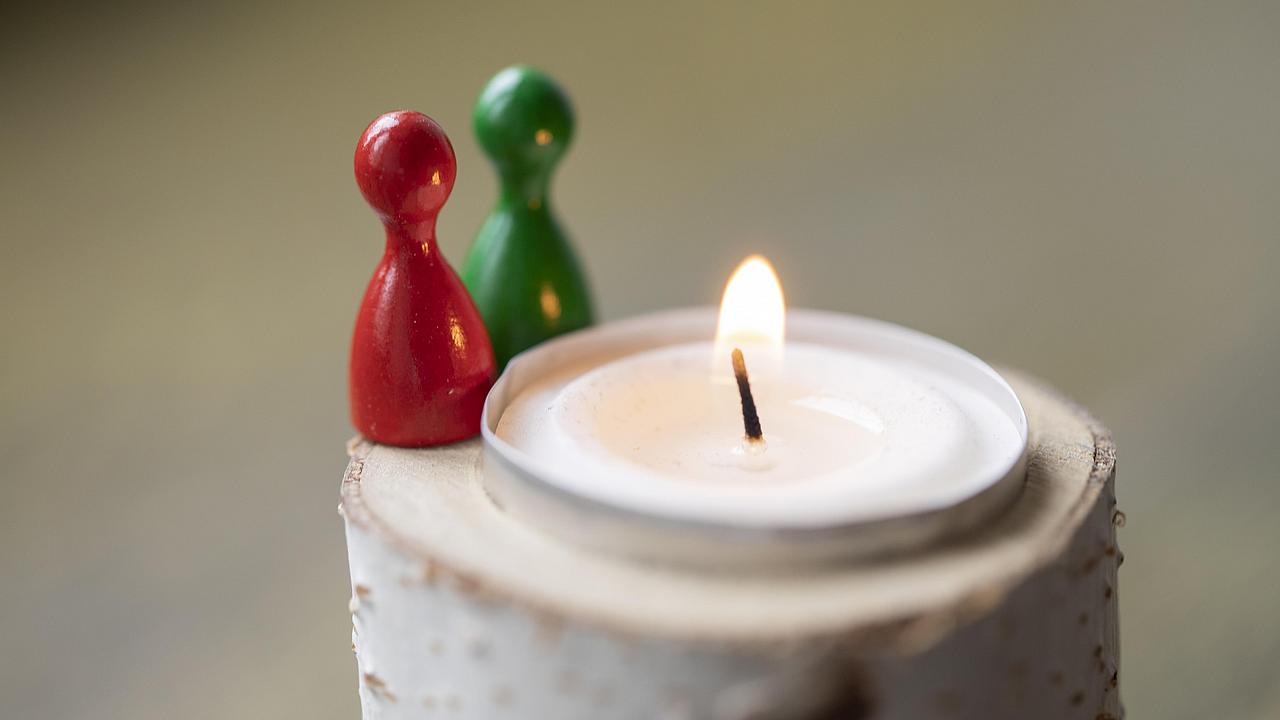 Zwei Figuren stehen neben dem wärmenden Licht einer Kerze