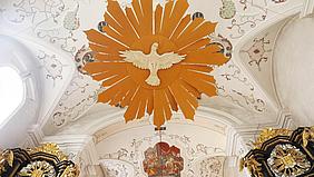 Eine große Holztaube hängt unter dem kirchendach als Sybol für den Heiligen Geist
