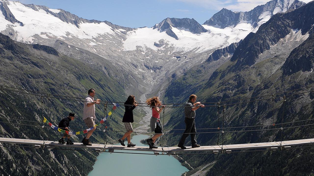 Vier Personen gehen auf einer Hängebrücke in einem Gebirge über einen Fluß
