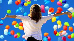 Frau steht vor fliegenden Luftballons.