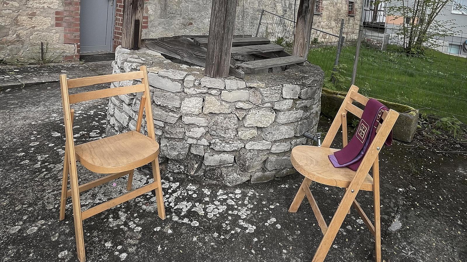 Symbolbild: Stühle mit Stola vor einem Brunnen.