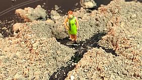 Miniaturfigur steht auf Teller mit Kreuz aus Asche